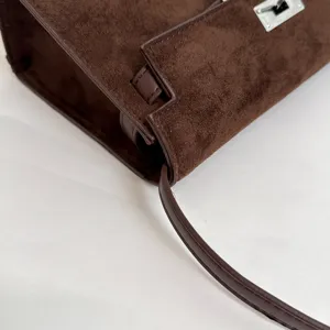 Bolso de mano de ante marrón con un elegante diseño estructurado, cierre metálico y correa.
