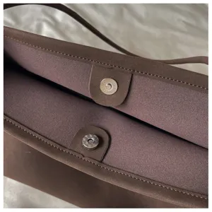 Detailed view of brown suede tote bag interior featuring magnetic snap closure and neat stitching.