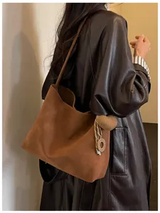 Close-up detail of a chic brown suede shoulder tote bag with elegant knitted charm pendant.