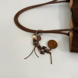 Detailansicht des braunen Wildleder-Shoppers mit Holzperlen-Anhänger und edlem Schulterriemen.