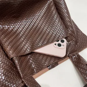 Close-up view of dark brown woven leather tote bag highlighting fine texture and front pocket.