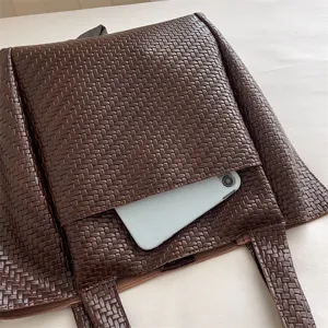 Brown woven leather tote bag detail highlighting the convenient front pocket and fine texture.