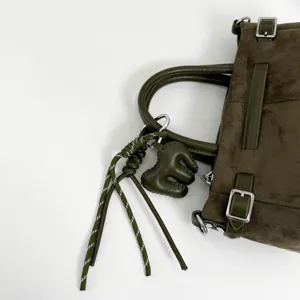Détail de sac à main en suédine vert olive avec boucles élégantes, poignées et charm tressé.