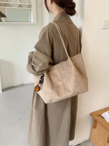 Detailansicht der großen Wildleder Schultertasche in Beige mit feiner Textur und Anhänger.