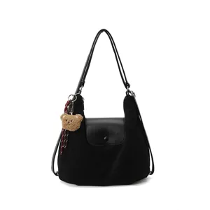 Minimalist black shoulder bag with stylish flap closure and cute teddy bear charm for daily commute.