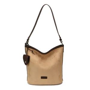 Close-up detail of khaki suede shoulder bag with brown leather strap and brand patch.