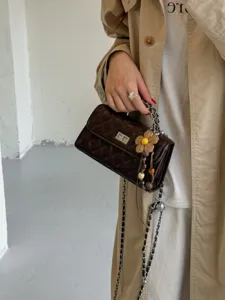 Close-up detail of a dark brown quilted chain crossbody bag featuring chic flower charm.