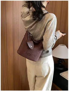 Detail shot of a brown suede hobo shoulder bag worn by a model, showing texture and strap.