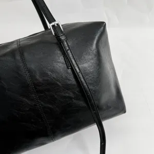 Black leather boston bag detail showing shoulder strap and metallic buckle design.
