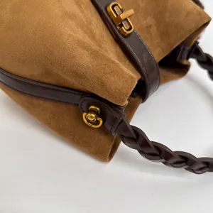 Vista dettagliata di una borsa a secchiello vintage in camoscio marrone con manico intrecciato e oro.