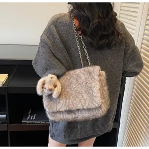 Détail de sac à bandoulière en peluche duveteuse avec chaîne en métal et pendentif animal.