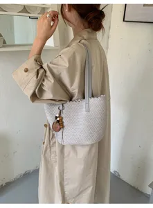 Detailed view of grey woven underarm bag with chic scalloped edge and charm pendant.