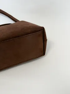 Brown suede shoulder bag detail shot showcasing fine stitching texture and material quality.