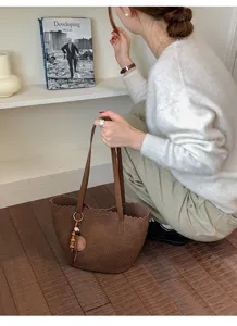 Close-up detail of the brown woven shoulder bag showcasing texture, wavy edge, and wooden charm.