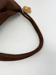 Detailed close-up of brown suede shoulder bag strap featuring a cute woven flower charm.
