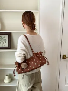 Brown polka dot shoulder bag with cute furry ball pendant, casual minimalist design detail.