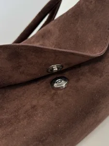 Brown suede shoulder bag detail showcasing durable magnetic snap closure and soft texture.