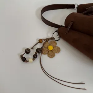 Nahaufnahme der braunen Wildleder-Beuteltasche mit gewebtem Blumenanhänger und Holzperlen.