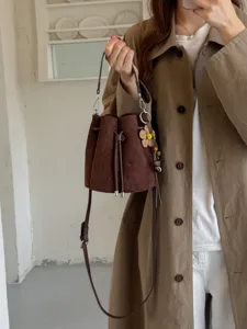 Nahaufnahme einer retro braunen Wildleder-Eimer-Tasche mit Kordelzug und einem gewebten Blumen-Anhänger.