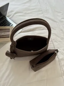 Detailed view of the vintage brown suede shoulder bag and matching pouch on cozy bedding.