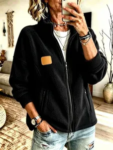 Detalle de chaqueta polar negra para mujer con cuello alto y parche de cuero.