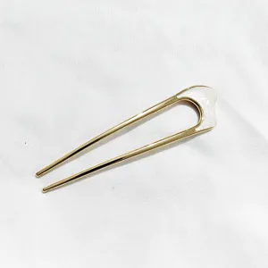 Gros plan sur la fourche à cheveux en métal doré en U avec détail blanc élégant.