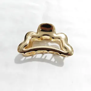 Golden metal hair claw clip, wavy cutout design detail, elegant hair accessory for styling.