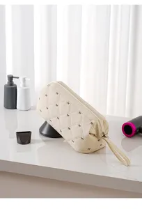Beige quilted hair dryer storage bag with cute bow embroidery, portable travel pouch design.