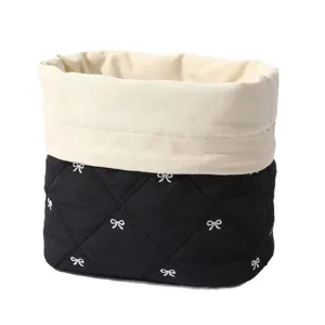 Black quilted cosmetic bag with white bow embroidery and beige canvas top storage basket.