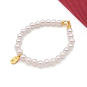 Close-up of elegant faux pearl bracelet with gold metal clasp and lucky charm pendant detail.