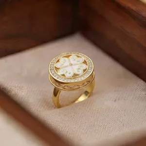 Primer plano de un anillo dorado con motivo de trébol, esmalte blanco y circonitas brillantes.