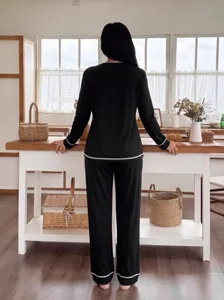 Detailed view of women's cozy black long sleeve pajama set with white piping in home scene.