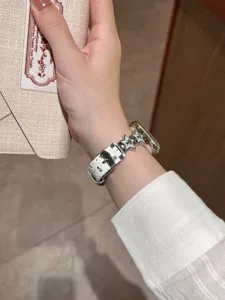 Detailaufnahme eines schmalen weißen Lederuhrarmbands mit sternenförmigen Metallanhängern.