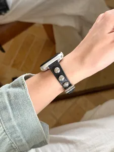 Cinturino per orologio in pelle nera con borchie metalliche, dettaglio del polso.