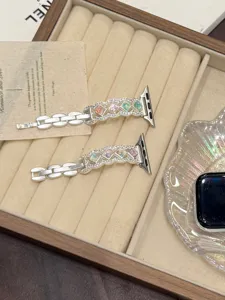 Detail shot of metal watch straps with colorful gemstone rhombus design on velvet tray.
