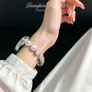 Close-up of metal watch strap with pink enamel clover charms worn on wrist detail view.