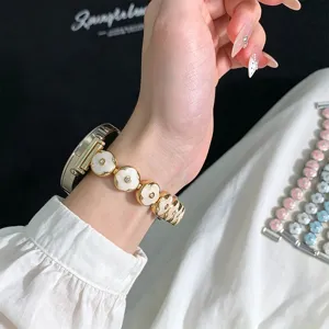 Metal clover watch strap detail showing white enamel flowers and gold links on wrist.