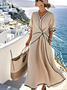 Elegante beige maxi-jurk met zwarte contrastrand, v-hals en chique knoopdetail aan de voorkant.