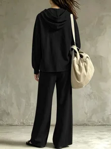 Back detail of casual black hoodie and wide leg pants two piece set against gray wall.