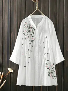 Detailed view of the white embroidered blouse, wooden background hanging style.