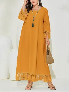 Detailed view of a stylish mustard yellow maxi dress with fringe hem and long sleeves.
