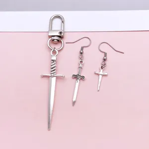Close-up detail of silver alloy sword pendant and punk style earrings set on pink background.