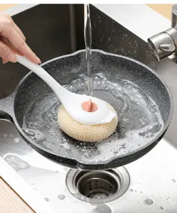 Detailed view of kitchen sponge brush cleaning frying pan in stainless steel sink with running water.