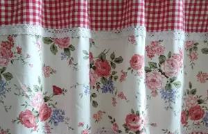 Fabric curtain detail closeup featuring charming red gingham, lace trim and pink roses pattern.