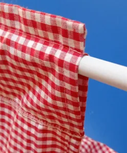 Close-up detail of red and white checkered fabric curtain hanging on a white rod.