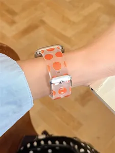 Gros plan détaillé d'un bracelet de montre en silicone translucide à pois orange porté au poignet.