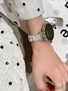 Metal watch strap detail showing irregular links with pink crystals for smartwatches.