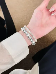 Gros plan détaillé d'un bracelet de perles à double rang et perles argentées texturées au poignet.