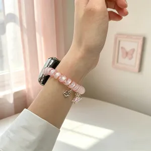 Vue détaillée du bracelet Apple Watch fil téléphonique rose avec charmantes pampilles papillon.