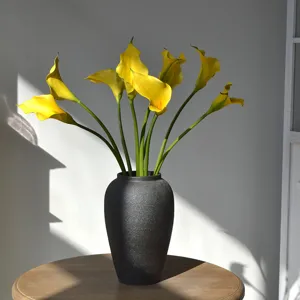 Vue detaillee de l'arrangement de fleurs artificielles lys calla EVA jaunes dans un vase texture.